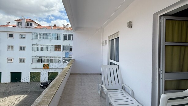 Un balcón con dos sillas de plástico blanco, una mesa pequeña y una ventana con cortina.