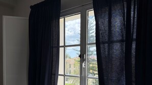 Una habitación con ventana, cortinas blancas y una silla blanca.