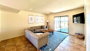 A living room with a sofa, a coffee table, and a rug. There are framed pictures on the wall and a window with a view.