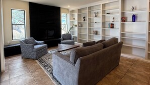 A living room with a fireplace, a sofa, a coffee table, a patterned rug, and a bookshelf.