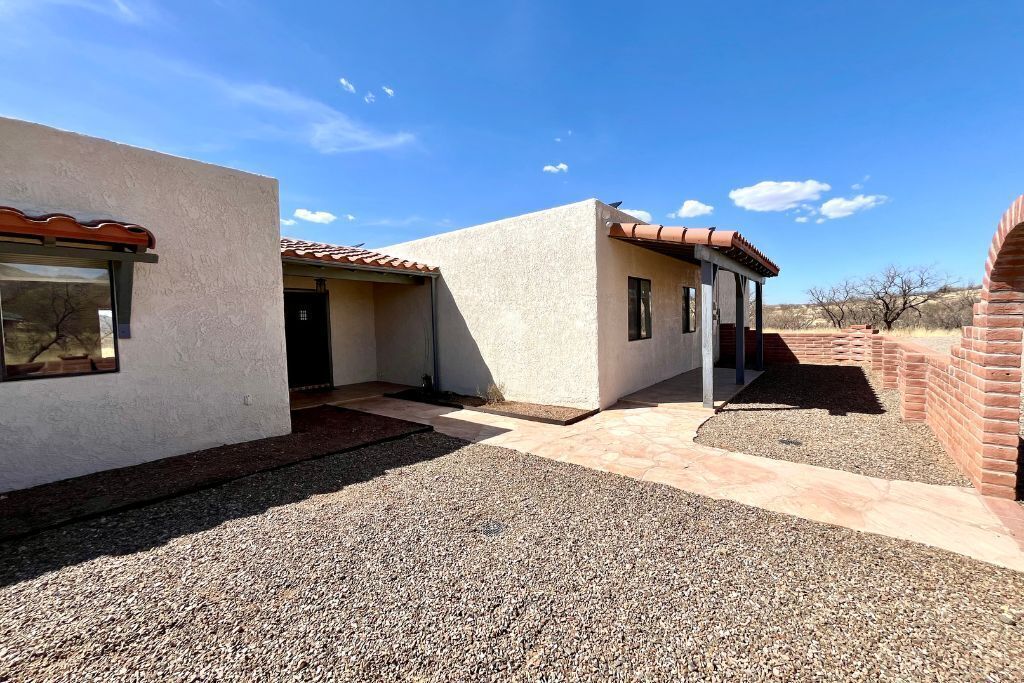 A modern building with a gravel driveway, a covered patio, and a brick structure in the background.
