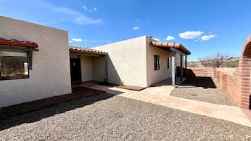 A modern building with a gravel driveway, a covered patio, and a brick structure in the background.