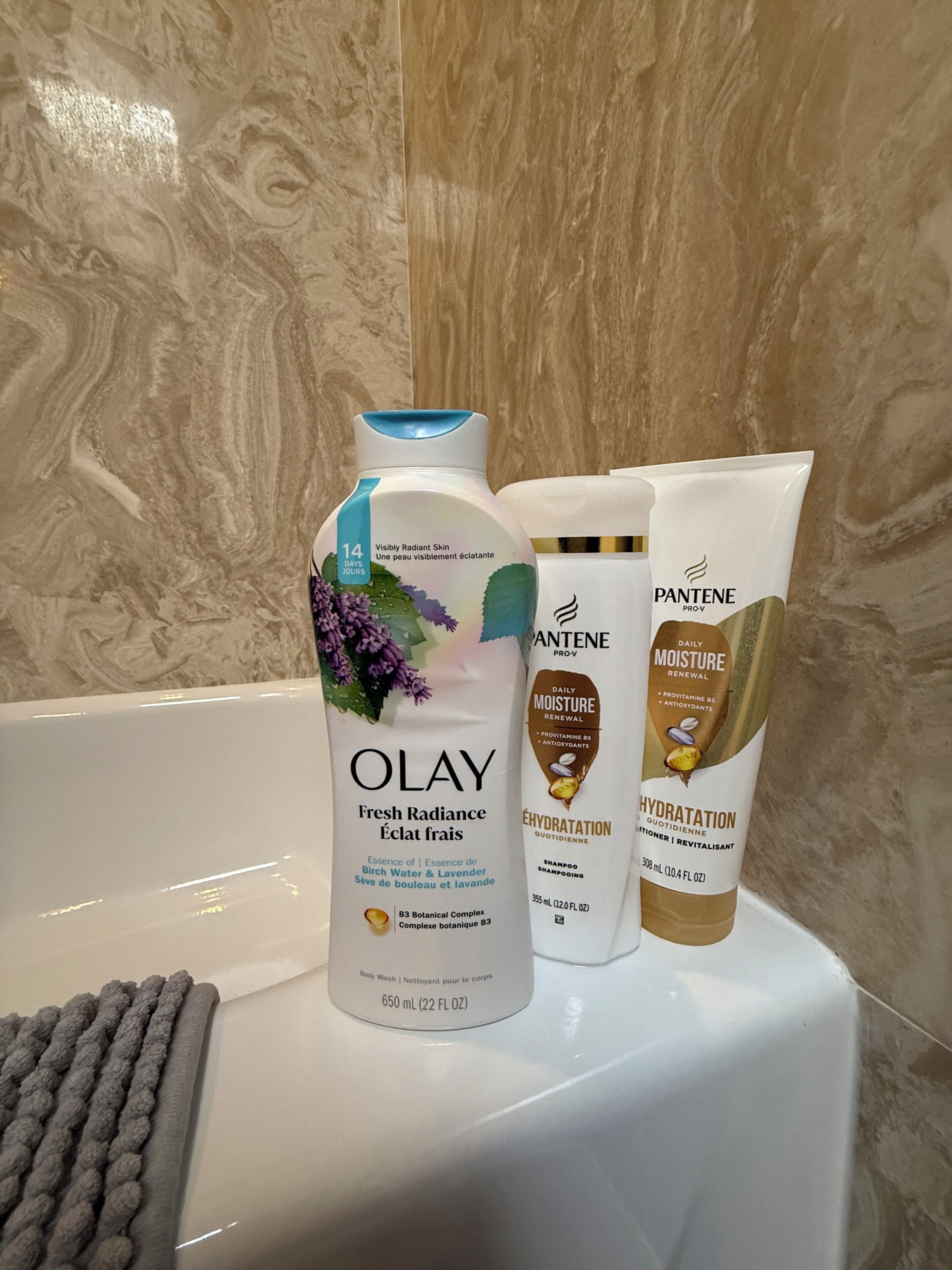 A bathroom with a marble wall, a white bathtub, and three toiletry bottles.