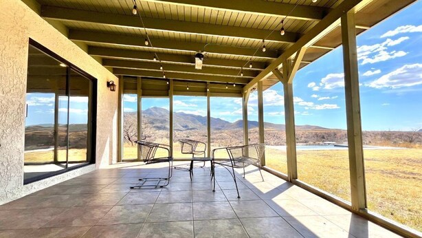 A covered patio with a view of mountains, metal chairs, and a tiled floor.