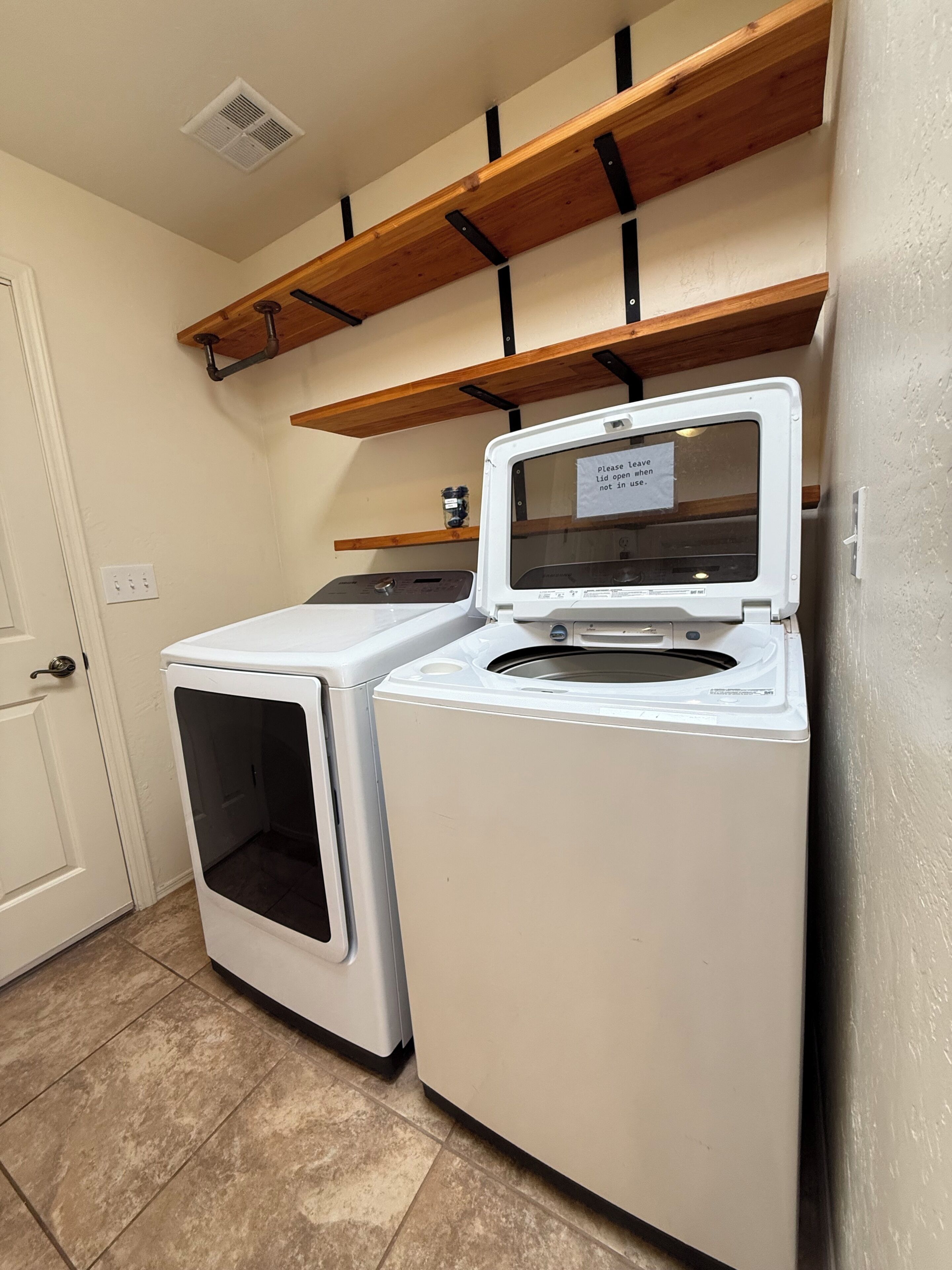 A laundry room with two stacked washers and dryers, wooden shelves above, and a white door.