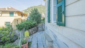 A narrow stone pathway leading to a building with green shutters and a bench. - Central Cozy Nest With Parking Bogliasco (Bogliasco)