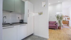 A modern kitchen with white cabinets, a sink, and a coffee maker. There is a purple sofa and a potted plant in the adjacent living area. - Central Cozy Nest With Parking Bogliasco (Bogliasco)