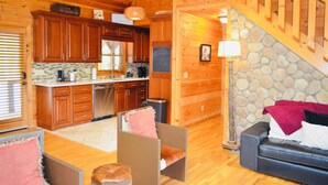 Interior de una cabaña de madera con cocina, sala de estar y una escalera de piedra.