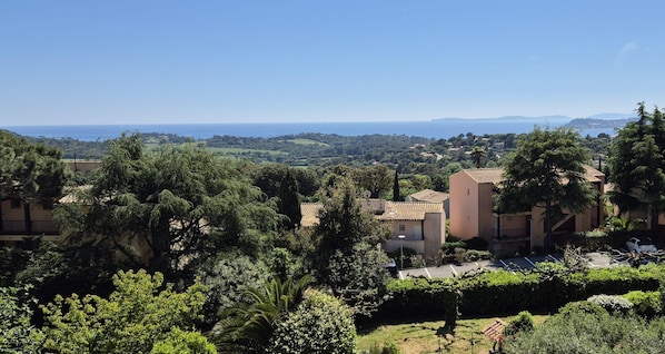 A residential area with Mediterranean-style buildings, lush greenery, and a view of the sea.
