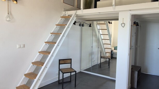 Ein mehrgeschossiges Interieur mit einer weißen Treppe, einem Sessel und einem Bett in der oberen Etage.