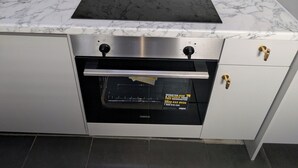 A kitchen with a black stovetop, a stainless steel range hood, a built-in oven, and a marble backsplash.