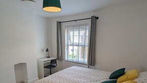 A bedroom with a bed, a desk, and a window with curtains.