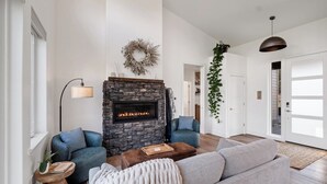 Una sala de estar moderna con chimenea de piedra, dos sofás, una mesa de centro y una planta colgante.