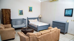 Una habitación con una cuna, una cama, un sofá, un aparador y dos cuadros colgados en la pared.