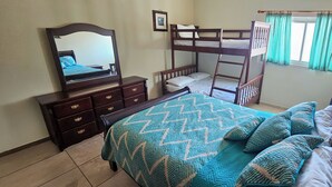 Un dormitorio con literas, un aparador con cajones, un espejo y una ventana con cortinas.