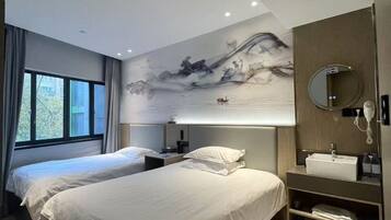 A modern hotel room with two beds, a large artwork on the wall, a bedside table with a lamp, and a built-in shelf with towels.