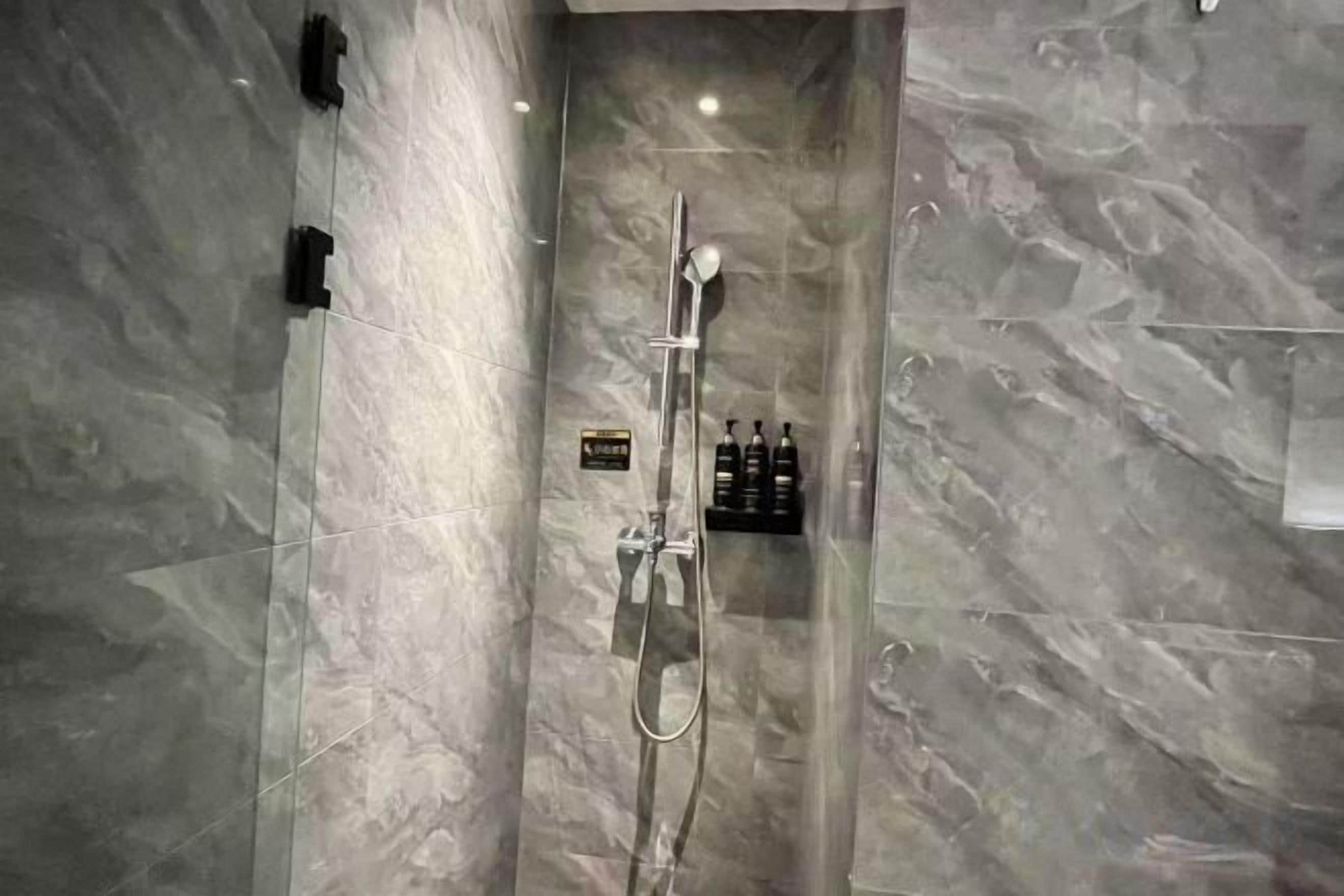A modern bathroom with a glass-enclosed shower, marble walls, and a shelf with toiletries.