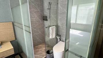 A modern bathroom with a glass-enclosed shower, a toilet, and a wooden bench.