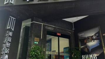 A hotel entrance with a glass door, a sign above the door, and a poster on the right side.