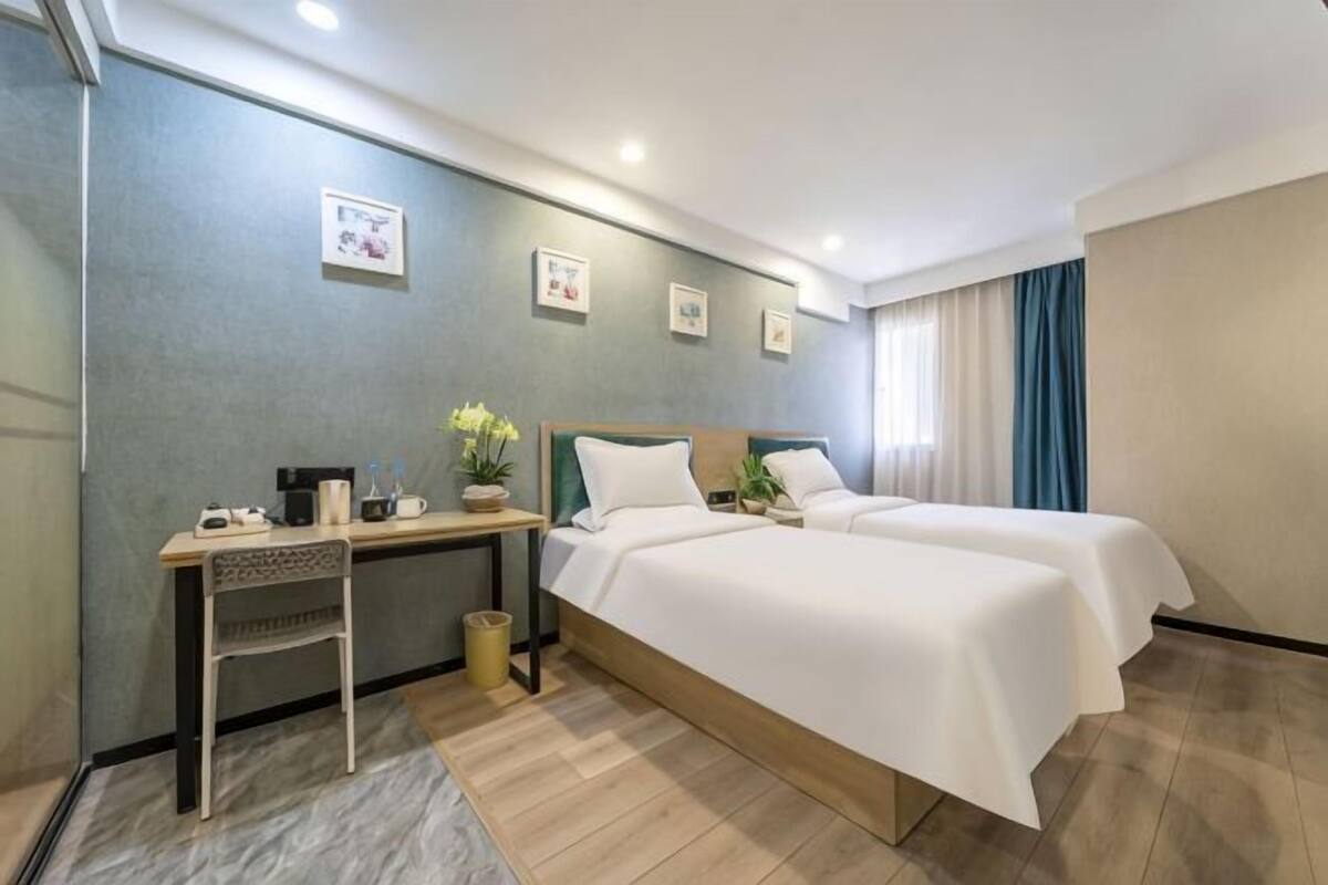 A hotel room with two beds, a desk, a chair, and a small table with a plant.