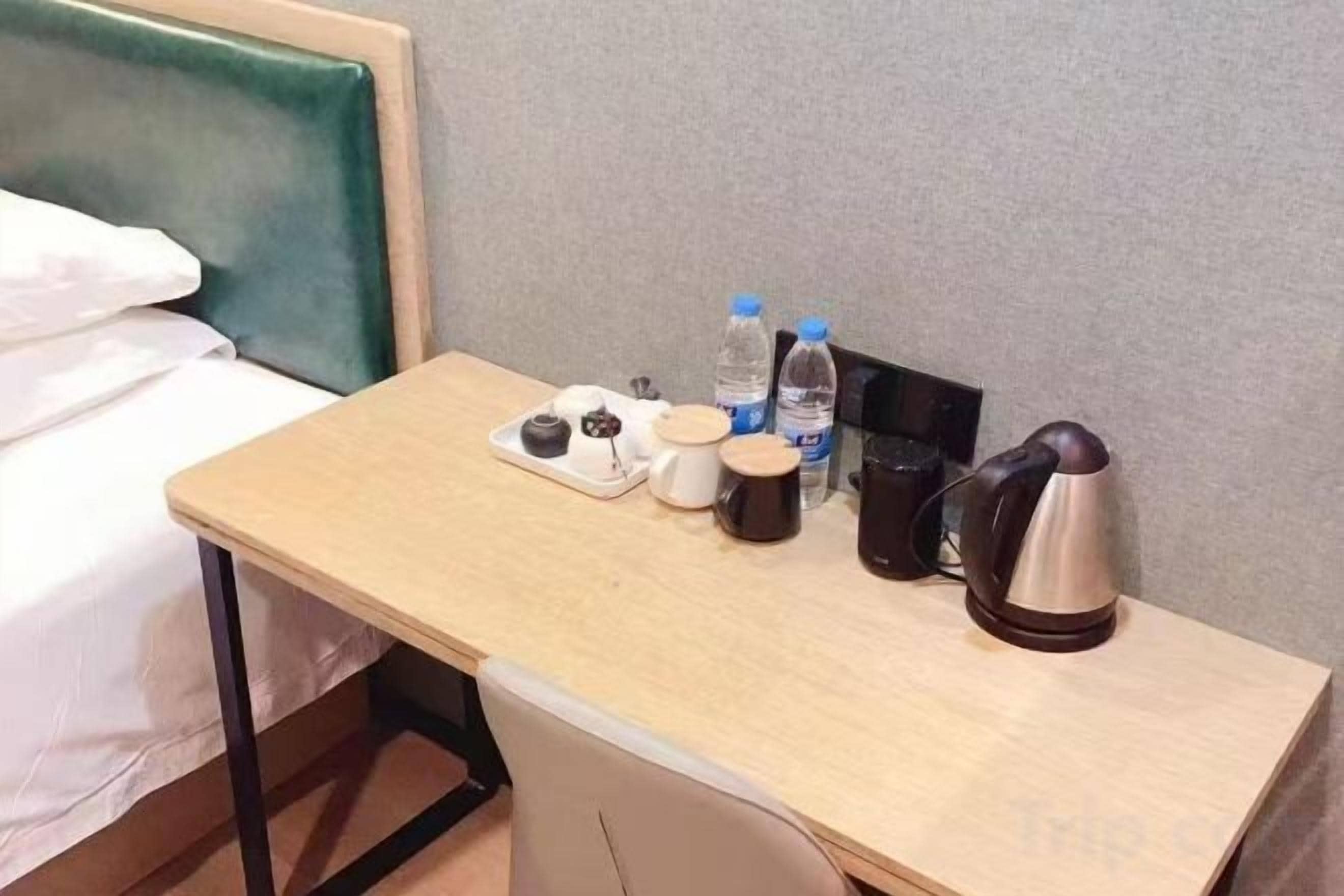 Ein Hotelzimmer mit einem Bett, einem kleinen Schreibtisch mit Wasserkocher, einer Wasserflasche und einer Tasse.