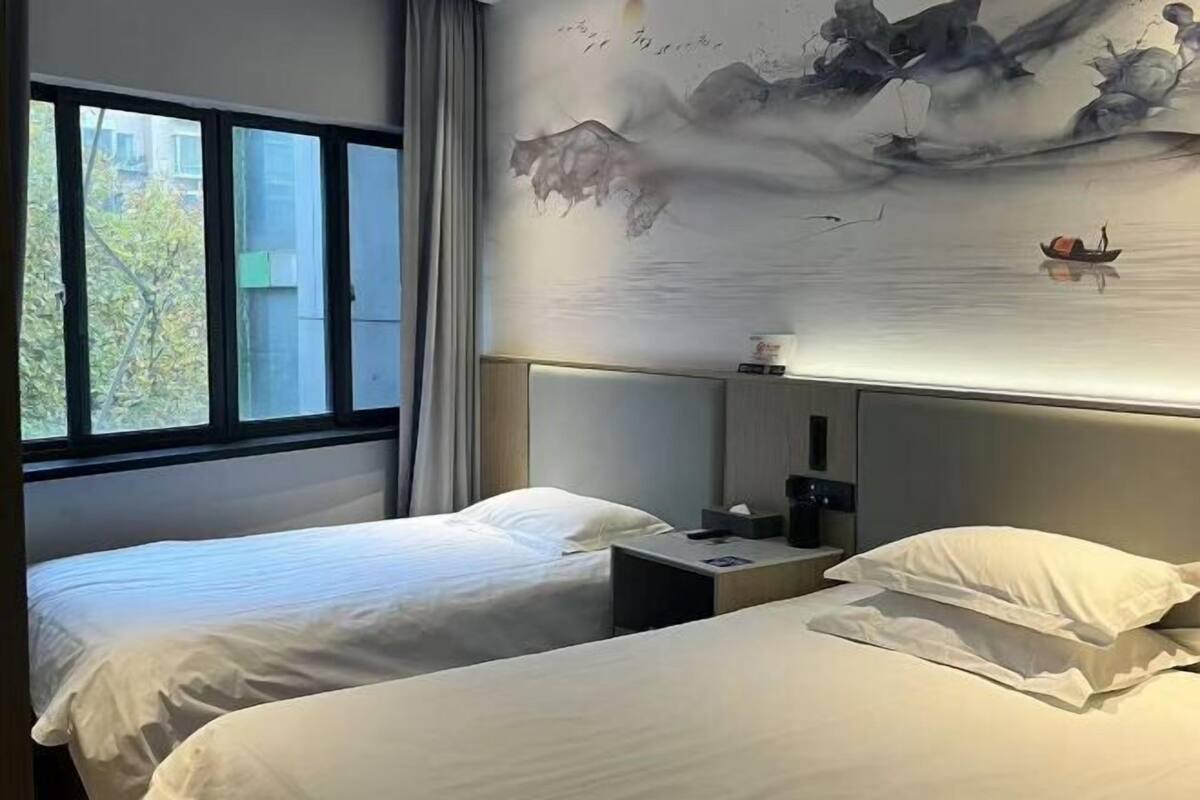 A hotel room with two beds, a large window, and a mural of a river scene on the wall.