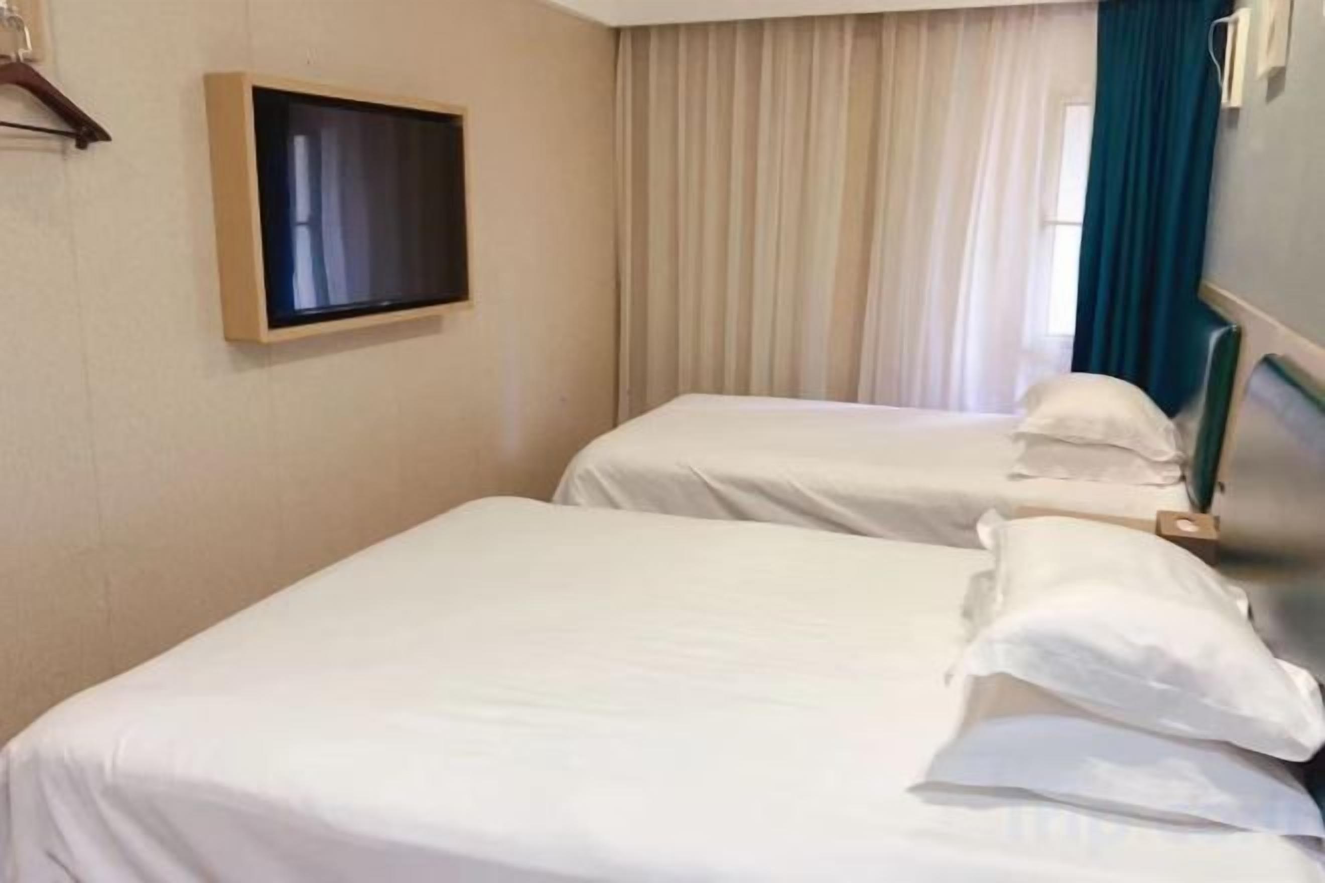 Habitación de hotel con dos camas, televisión y ventana con cortinas.
