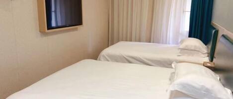 Habitación de hotel con dos camas, televisión y ventana con cortinas.