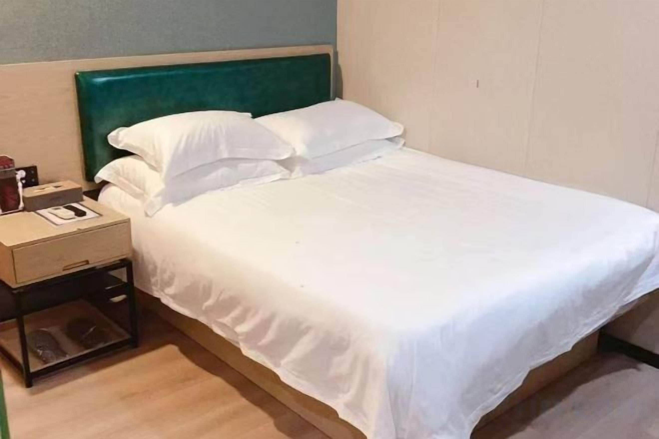 A single bed with white bedding, a wooden nightstand, and a teal headboard.