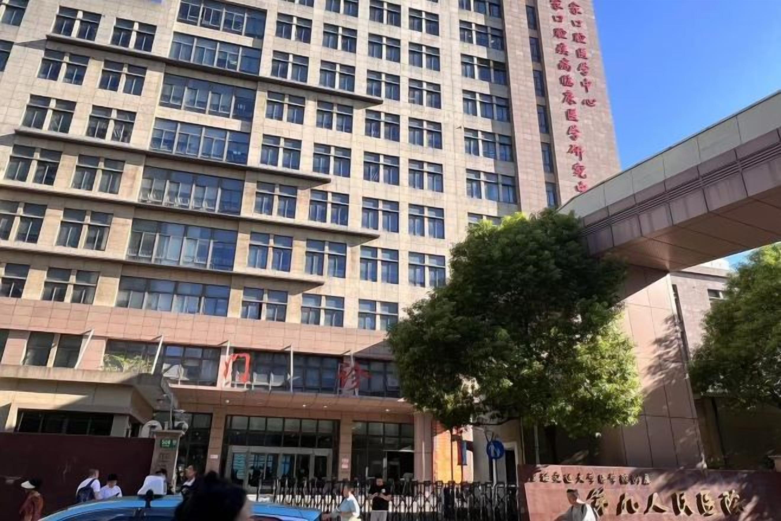 A multi-story building with a modern architectural design, featuring a prominent entrance and a large tree in front.