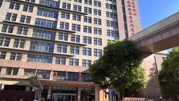 A multi-story building with a modern architectural design, featuring a prominent entrance and a large tree in front.