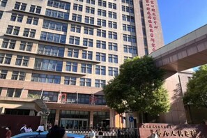 A multi-story building with a modern architectural design, featuring a prominent entrance and a large tree in front. - Waiting Qingju Hotel (9th People's Hospital Lujiabang Road Subway Station Branch) (Shanghai)