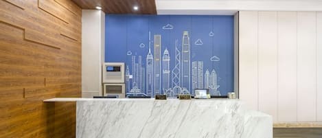 Un mostrador de recepción con encimera de mármol, un mural con vistas al horizonte de la ciudad y un panel de madera al lado izquierdo.