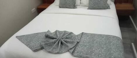 A neatly made bed with white sheets and gray pillows, a gray blanket, and a gray towel arranged on the bed.