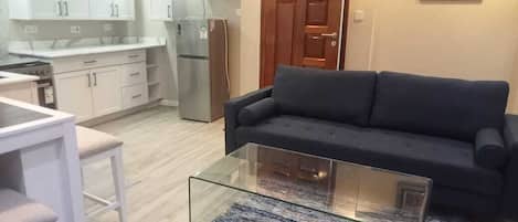 A compact living space with a kitchenette, a sofa, a glass coffee table, and a patterned rug.