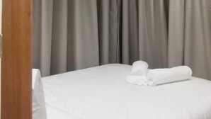 A hotel room with a neatly made bed, grey curtains, and a wooden headboard. - Kenzi Suites (Kisii)