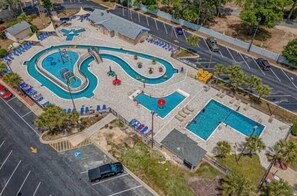 Vue aérienne d’un complexe de piscines comprenant plusieurs bassins et toboggans, entouré de chaises longues et de parasols.