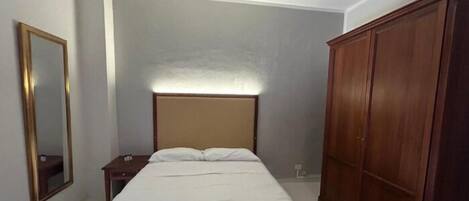 Un dormitorio con cama, mesita de noche, armario y espejo.