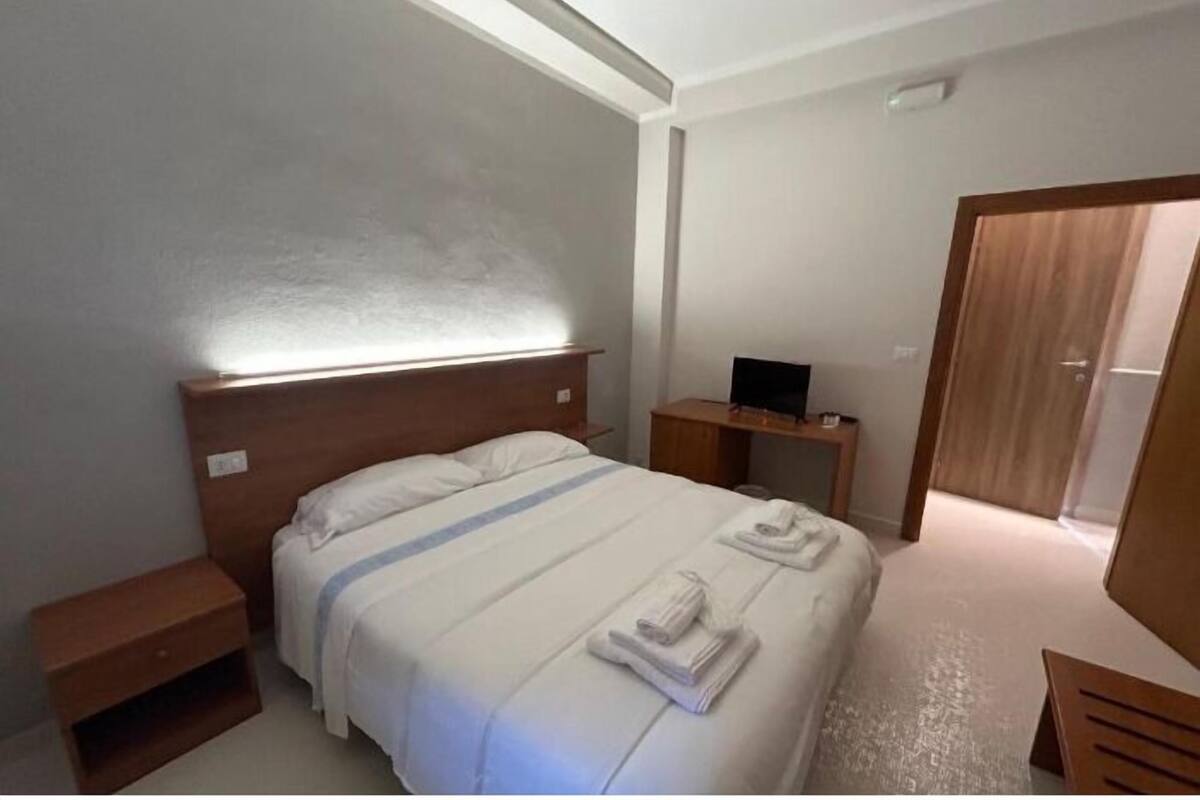 Una habitación de hotel con una cama grande, una mesita de noche, un televisor y un armario.