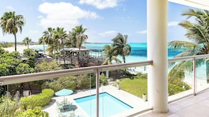 A balcony with a clear view of a pool, palm trees, and a beach.