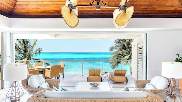 A modern lounge with wicker furniture, a glass coffee table, and a view of the ocean.