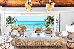 A modern lounge with wicker furniture, a glass coffee table, and a view of the ocean.