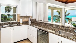 A kitchen with granite countertops, white cabinets, a built-in dishwasher, and a view of the ocean.