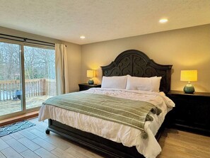 A bedroom with a large bed, two bedside tables with lamps, a sliding glass door to a balcony, and a wooden floor.
