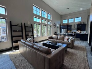 A spacious living room with a large sofa, a coffee table, and a kitchen area visible through the windows.
