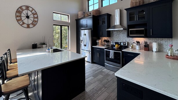 Une cuisine moderne avec des meubles de couleur sombre, des appareils électroménagers en acier inoxydable et un grand îlot central.