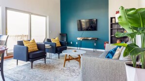 Un salon moderne avec un mur d’accent de couleur turquoise, un téléviseur à écran plat fixé au-dessus d’une table en bois et une grande plante verte.