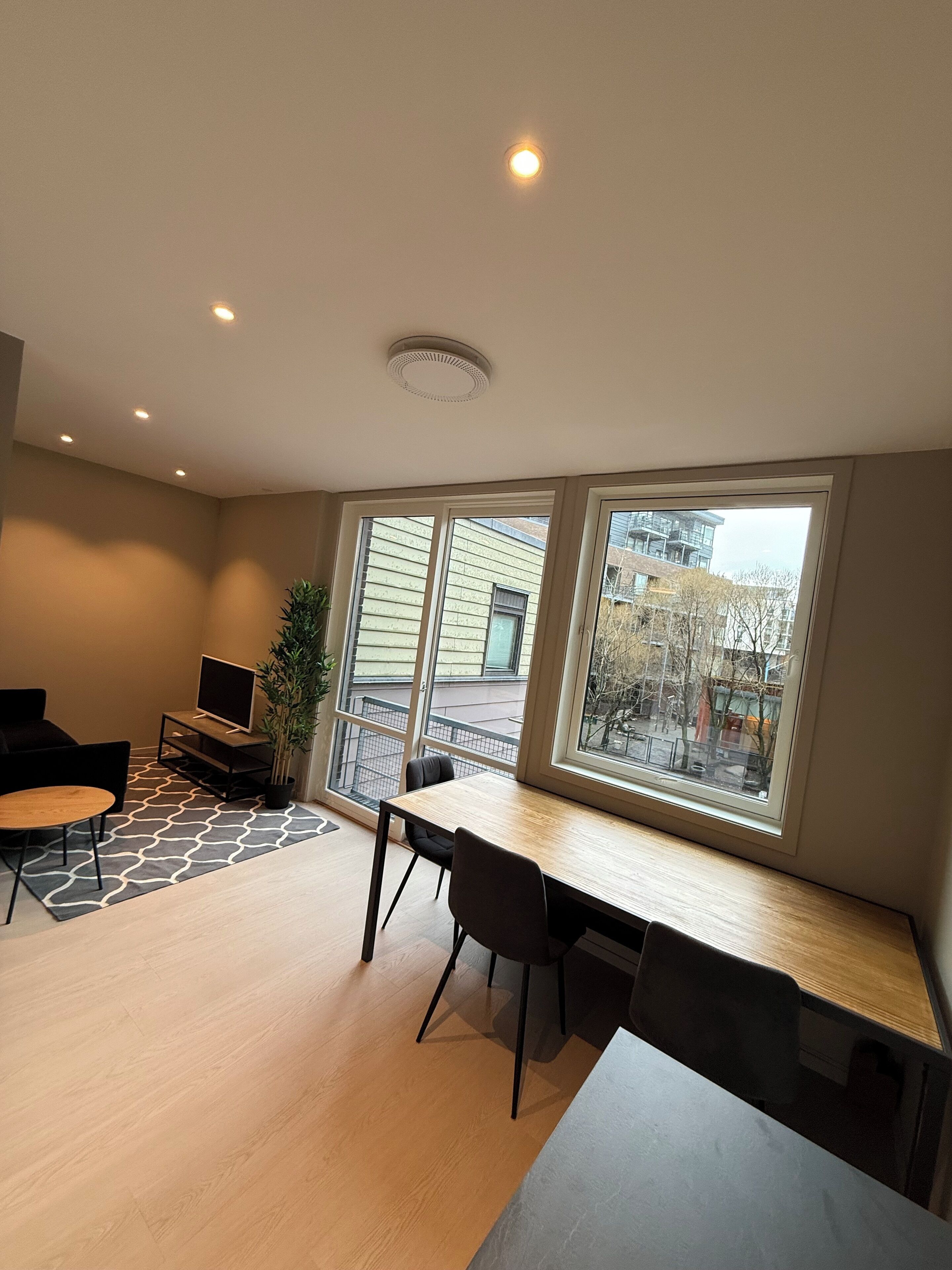 A modern living room with a dining area, large windows, and a view of the outside.