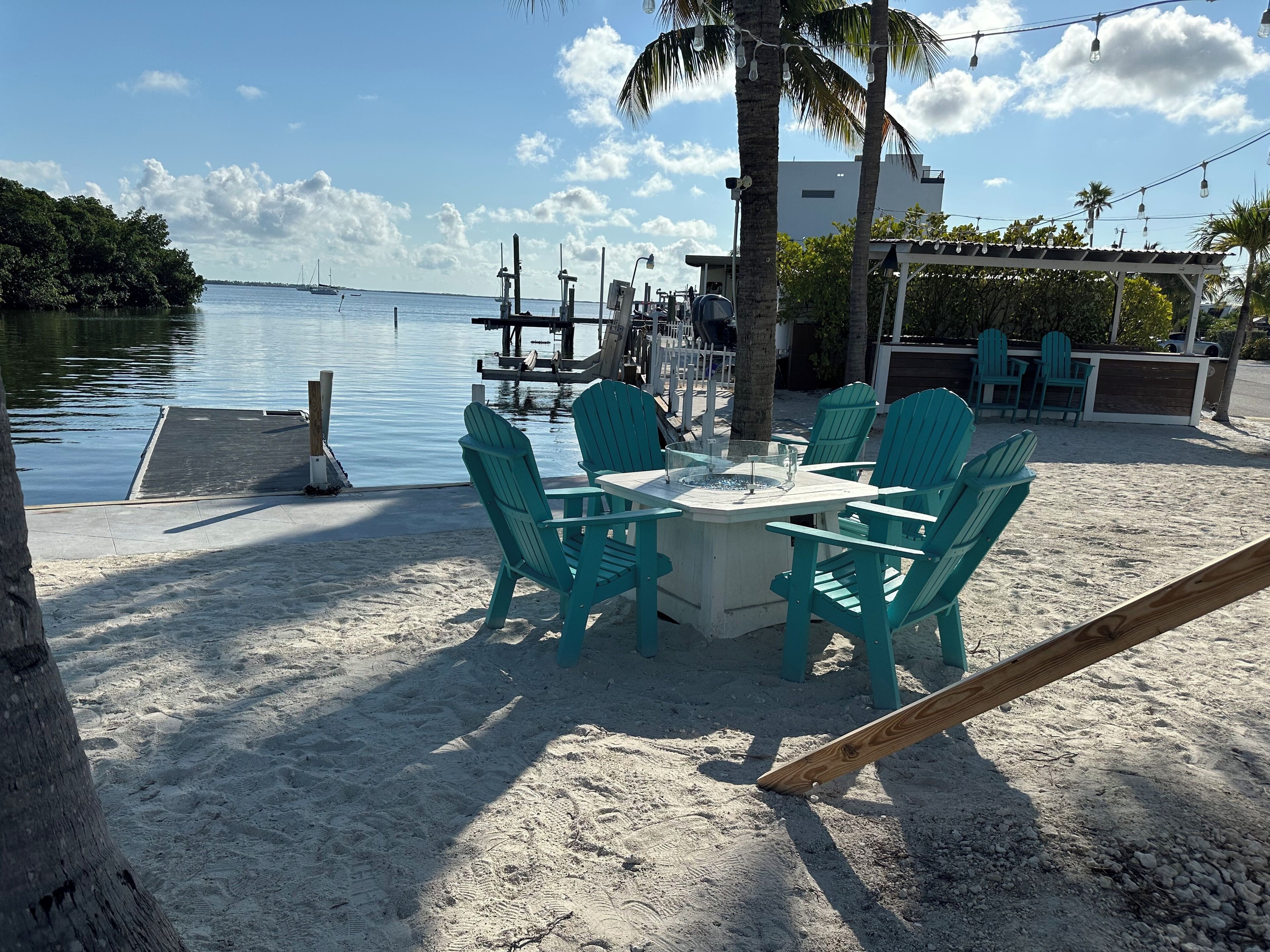 A beachside dining area with a table and chairs, a fire pit, and a view of the water.