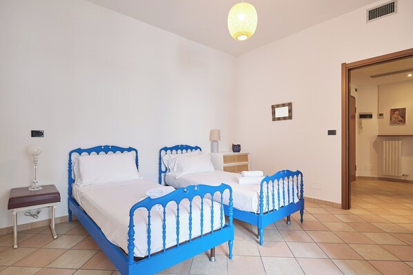 A bedroom with two beds, a nightstand, a lamp, and a door leading to another room.